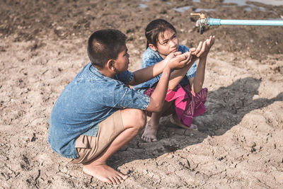 Siblings crouching by tap on drought field