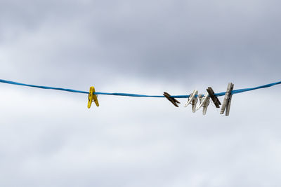 Low angle view of clothespins hanging on rope against sky