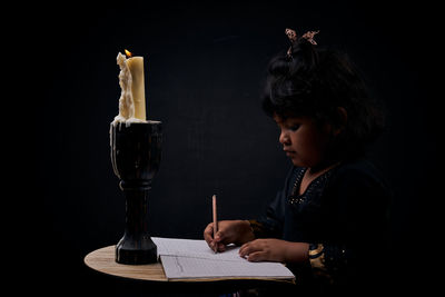 Portrait of girl holding table against black background