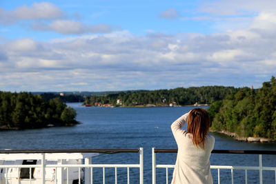 Rear view of woman standing by sea against sky