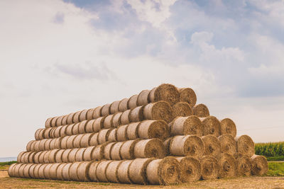 Stack of hay bales on field against sky