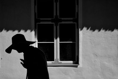 Rear view of silhouette person standing against window of building