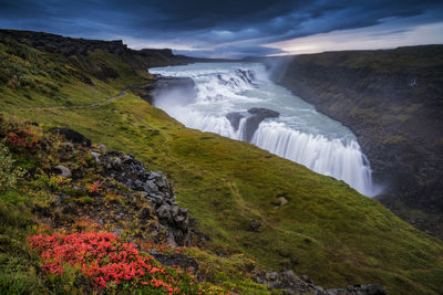 Scenic view of waterfall on cliff against sky