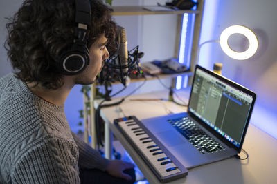 Young music composer with headphones and piano using laptop at home