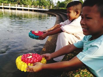 Smiling friends holding toys while sitting by lake