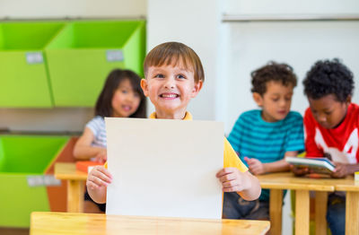 Smiling boy holding blank paper in classroom