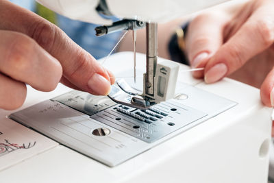 Cropped hands of tailor adjusting thread in sewing machine