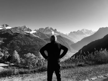 Rear view of man looking at snowcapped mountains against clear sky