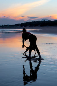 Silhouette woman on beach against sky during sunset