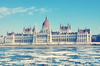 Frozen danube river by hungarian parliament building against blue sky