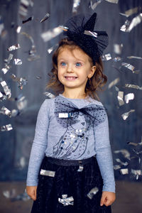 Portrait of a little girl  in the studio in a black mask and a big bow and falling silver confetti