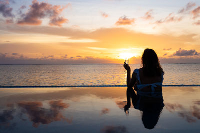 Attractive woman on a infinity pool near the ocean with a glass of champagne.back view