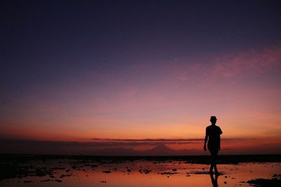 Silhouette man standing at beach against sky during sunset