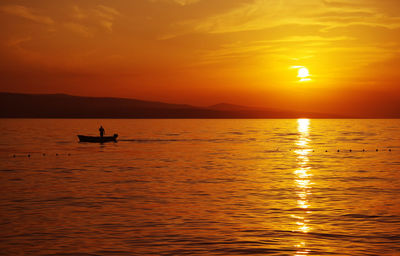 Silhouette person in sea against sky during sunset