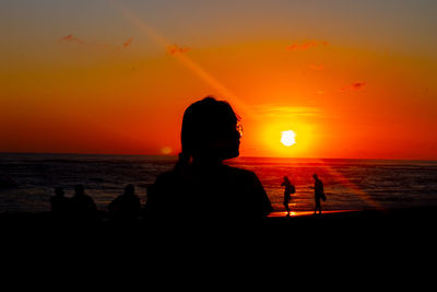 Silhouette people sitting on beach during sunset
