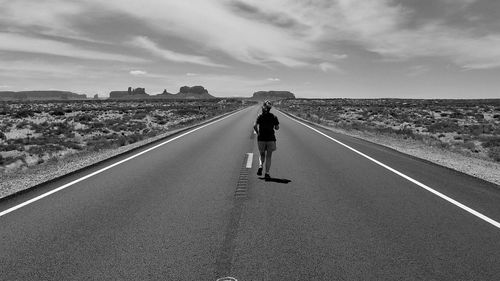 Rear view of man walking on road against sky