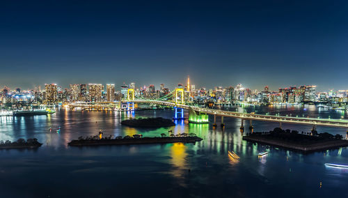 Illuminated bridge over river by buildings in city at night