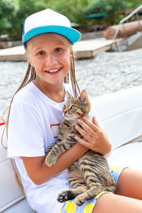 Teenager girl gently holds tabby kitten, looking at camera, smiling.