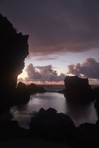 Lake amidst silhouette rocks against sky during sunset