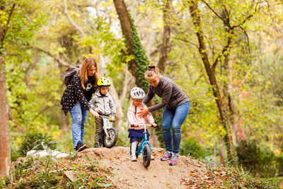 Full length of cute kids riding bicycle against trees