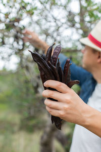 Man holding carob bean while standing outdoors