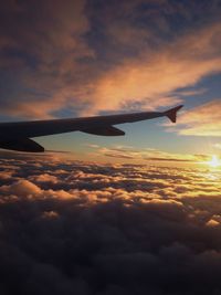Airplane flying over cloudscape against sky during sunset