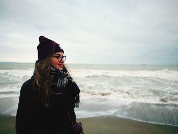 Side view of smiling young woman standing at beach against sky