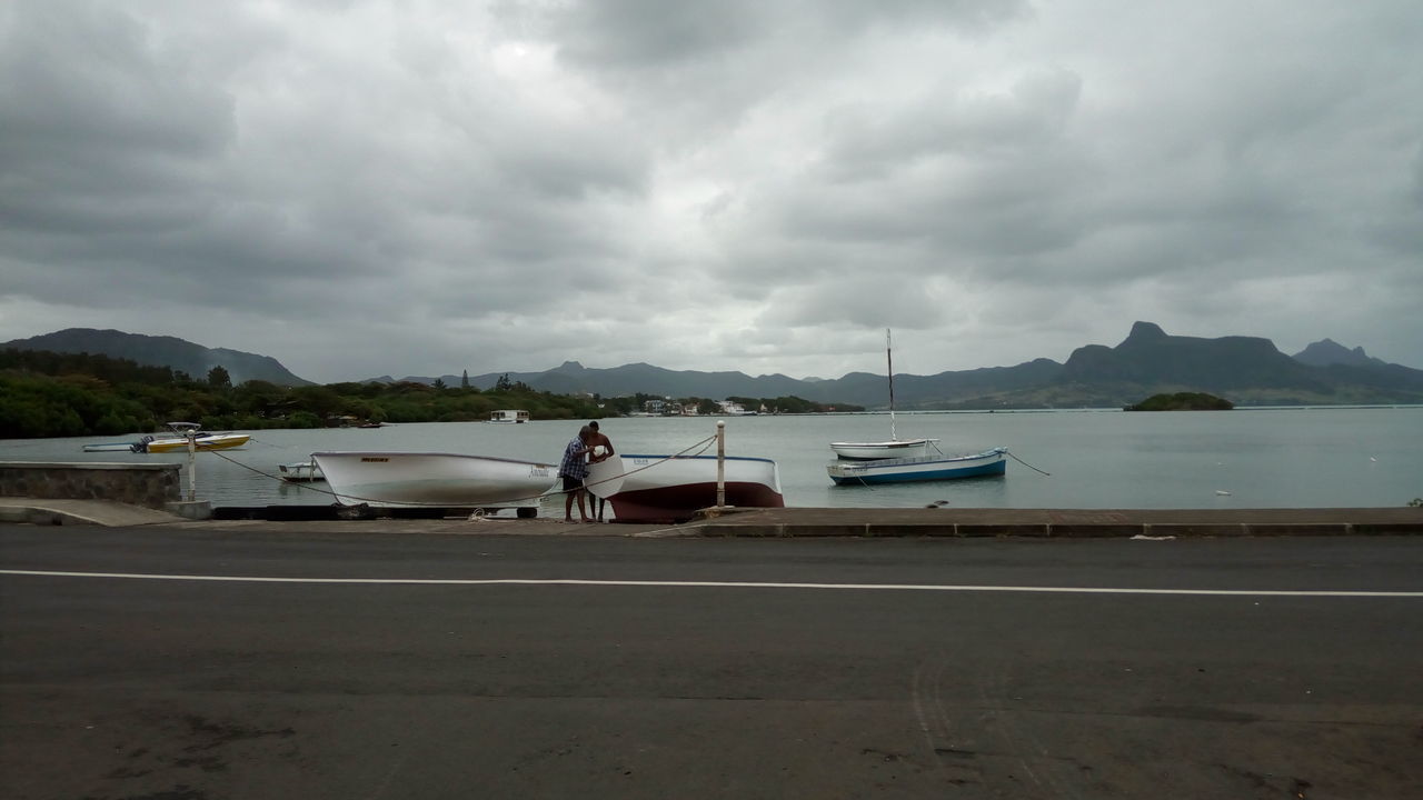 MAN STANDING ON BOAT MOORED AT BEACH