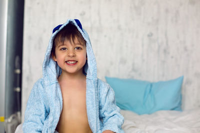 Portrait of a child in a blue robe sitting on a white bed after a bath