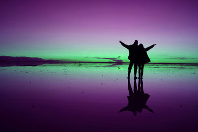 Silhouette couple standing on shore against sea during sunset