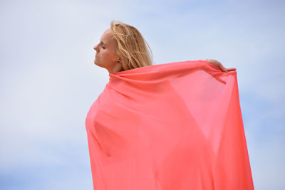 Young caucasian woman standing in desert against blue sky, covered with pink fabric.