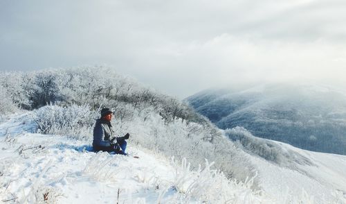 Man sitting on snow covered mountain against sky