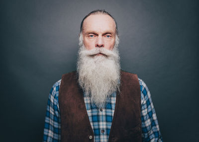 Portrait of confident senior man with long white beard against gray background