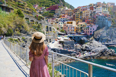 Woman with hat and dress walking along the promenade of manarola village in the cinque terre, italy