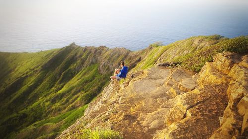 High angle view of man sitting on cliff by sea