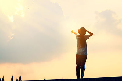 Rear view of woman standing at beach during sunset