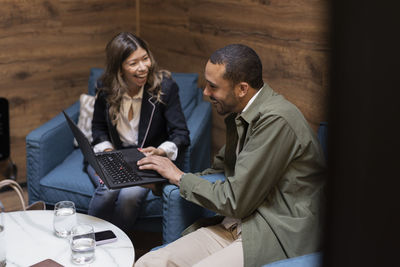 Cheerful business colleagues discussing over laptop while sitting in office