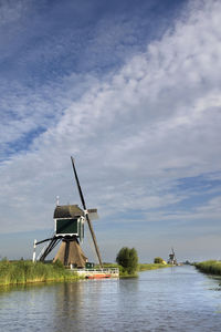 Traditional windmill by river against sky