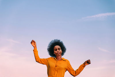 Woman with arms outstretched standing against sky