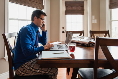 Man on cellphone working from home using a computer in pyjama pants.