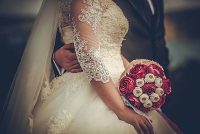 Midsection of bride holding bouquet with groom