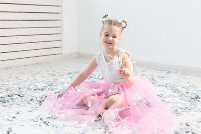 Portrait of smiling girl sitting against pink wall