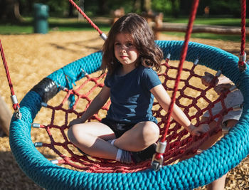 Portrait of a beautiful caucasian girl sits on a round rope swing in the park at the playground