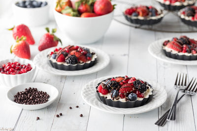 Individual homemade mixed berry cheesecake tarts on a white wooden table.