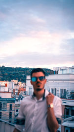 Young man standing by cityscape against sky