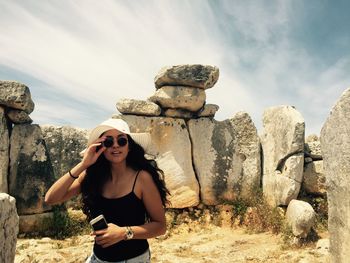 Portrait of young woman wearing sunglasses while standing against rocks