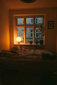 Bed by illuminated lamp on window sill at home
