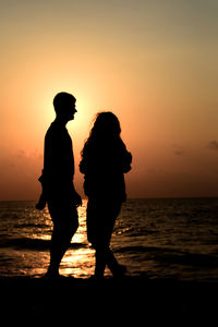 Silhouette couple standing on beach during sunset