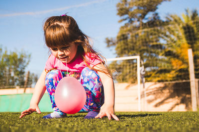 Cute girl with balloon crouching on turf