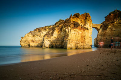 Rock formations on beach against clear blue sky